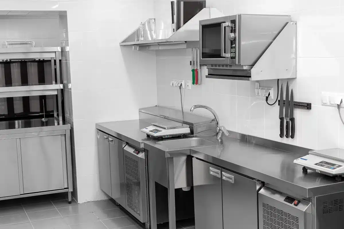 Cuisine professionnelle en acier inoxydable avec hotte, four à micro-ondes mural, évier, balances de précision et porte-couteaux magnétique.